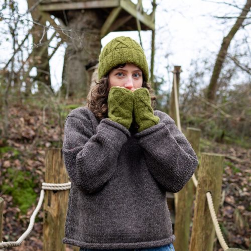 Woman wearing a wool jumper with green woollen hand warmers and hat outdoors in nature